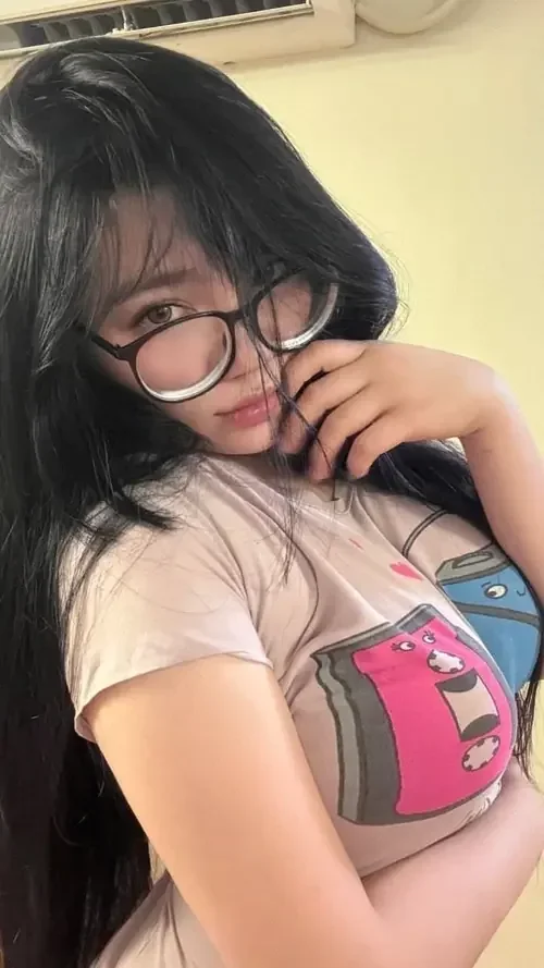 Người mẫu đeo kính mặc áo trắng in hồng, cúi nhẹ người để vú to tròn hiện rõ