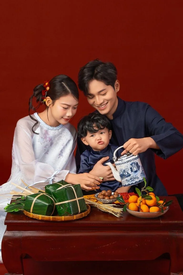 Gia đình quây quần gói bánh chưng trên bàn cùng mâm trái cây ngày Tết