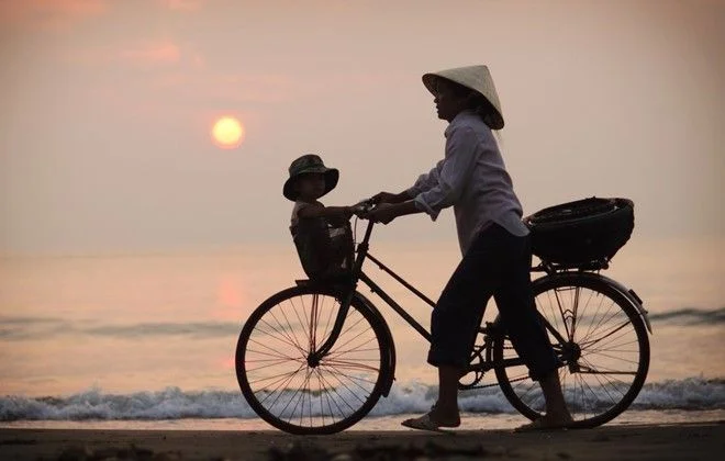 Mẹ chở con bằng xe đạp trên bãi biển lúc hoàng hôn
