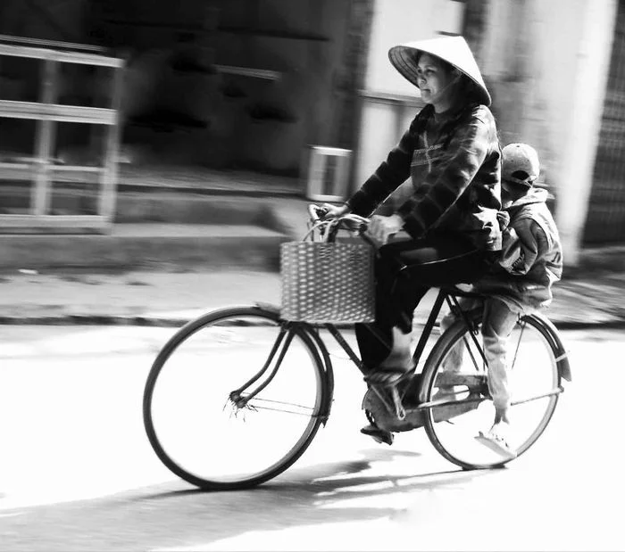 Người mẹ đội nón lá chở con trên chiếc xe đạp cũ trên đường phố